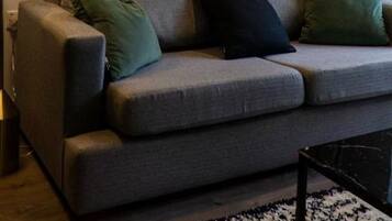 A living room with a sofa, two cushions, a lamp, and two framed pictures on the wall.