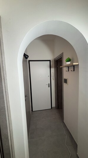A hallway with a white door, a small plant on a shelf, and a wall-mounted telephone. - A comfortable apartment right in the heart of the city and just a few meters from the sea (Castellammare del Golfo)