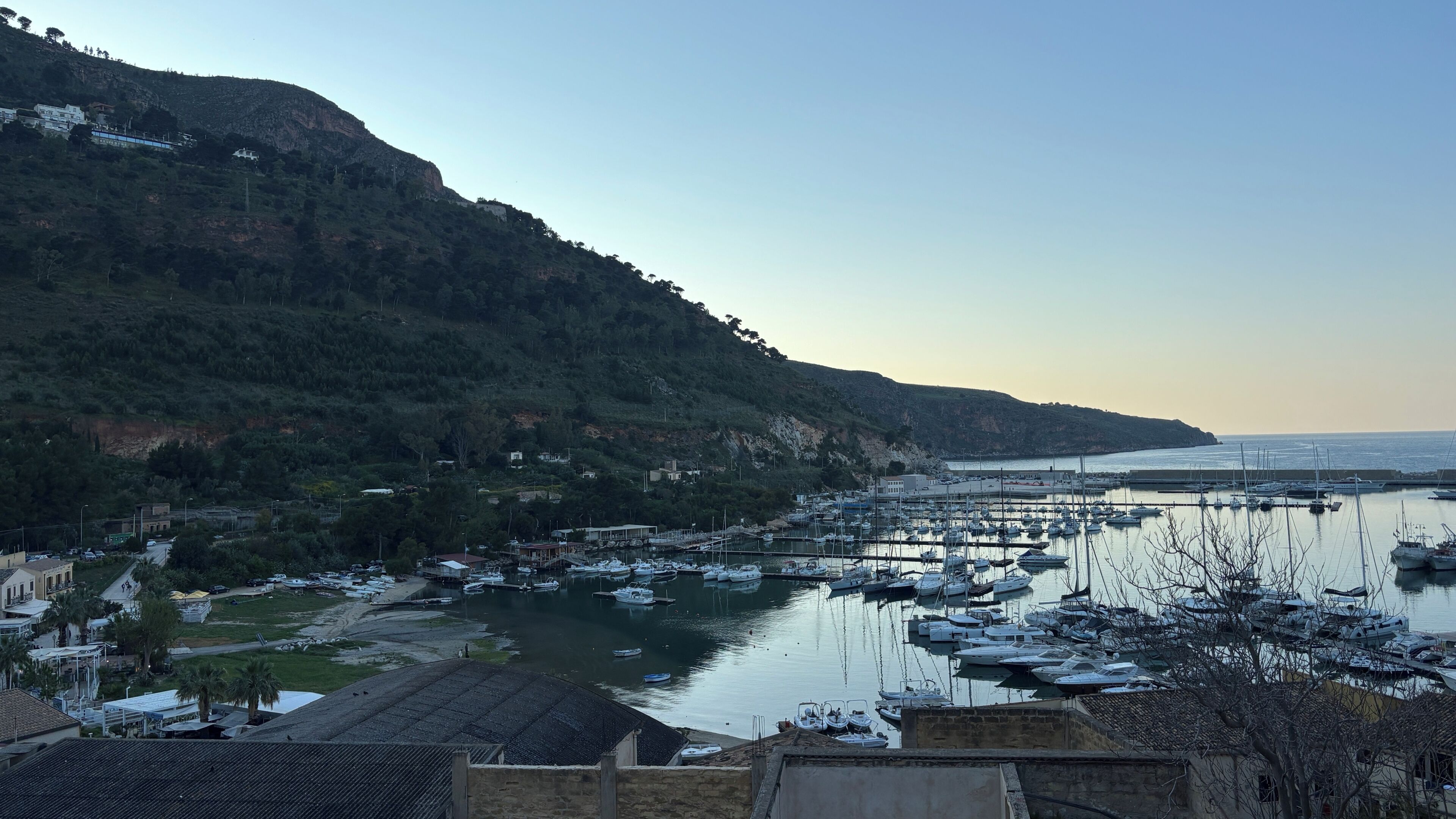 Un port de plaisance avec des bateaux amarrés, un paysage vallonné en arrière-plan et des bâtiments le long de la rive.