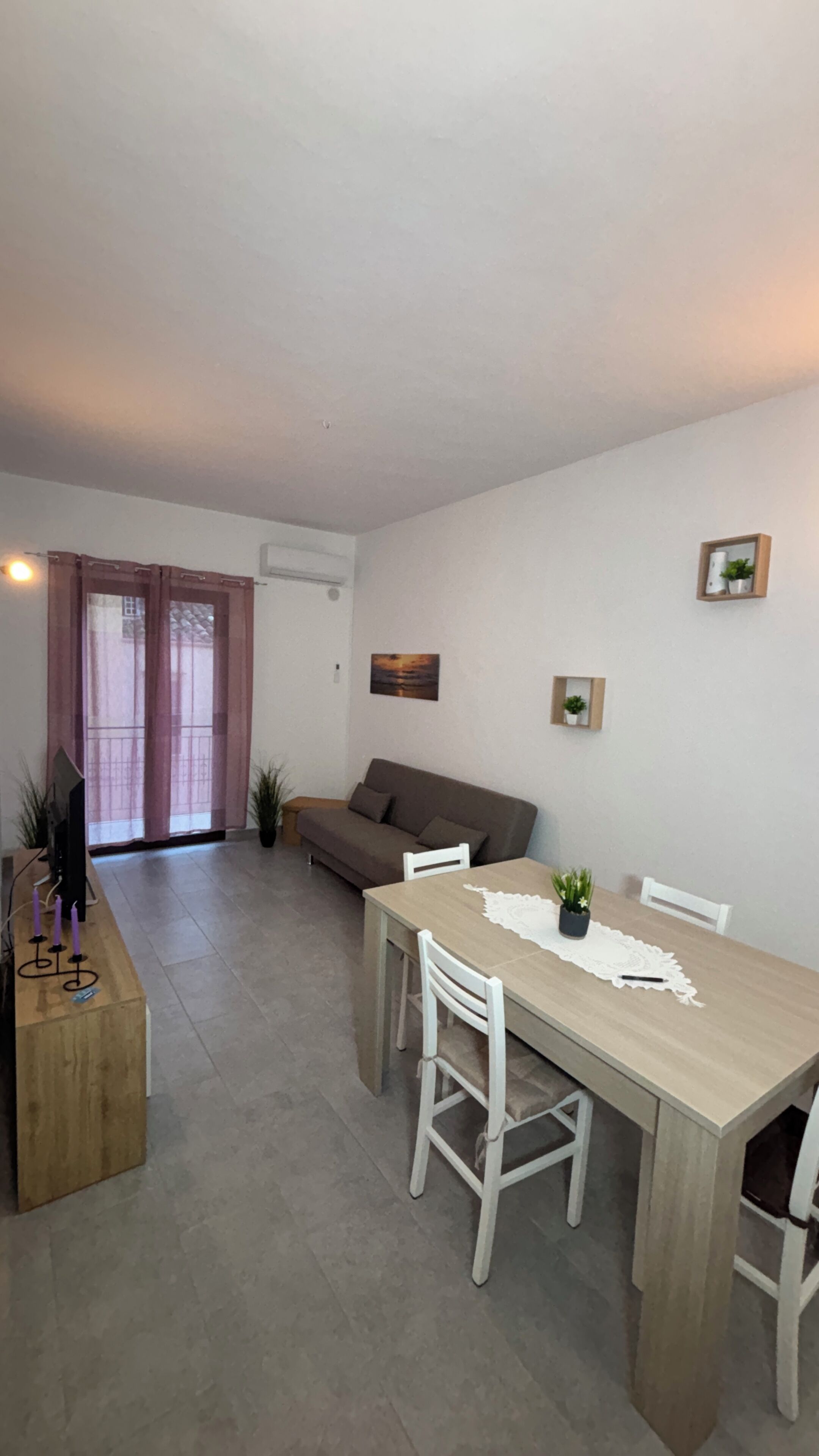 Un salon comprenant un canapé, une table à manger avec des chaises, un téléviseur et une fenêtre avec des rideaux.