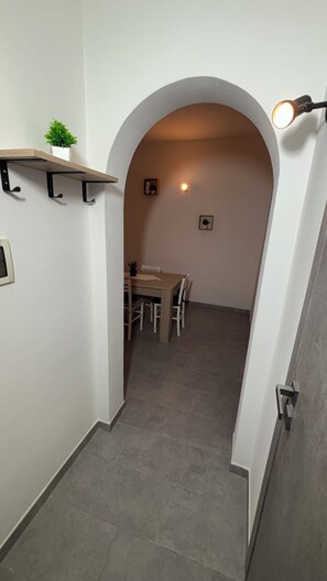A hallway with a dining area at the end, featuring a table and chairs, a small plant on a shelf, and a light fixture above the door. - A comfortable apartment right in the heart of the city and just a few meters from the sea (Castellammare del Golfo)