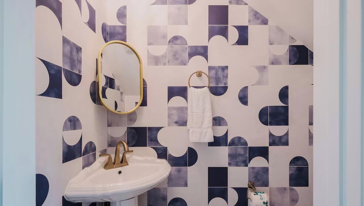 A bathroom with a white sink, gold faucet, and a mirror with a gold frame.