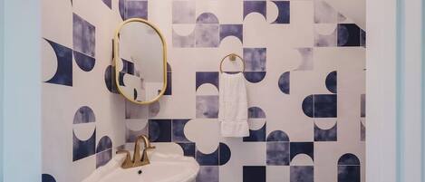 A bathroom with a white sink, gold faucet, and a mirror with a gold frame.