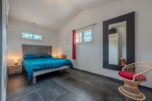 A bedroom with a bed, bedside table, lamp, window, and a chair.