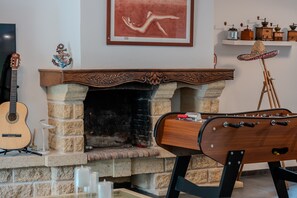 Quarto com lareira, um violão, uma obra de arte emoldurada e uma estante com diversos objetos.