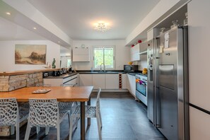 A modern kitchen with a dining area, featuring a stone accent wall, a large window, and stainless steel appliances.