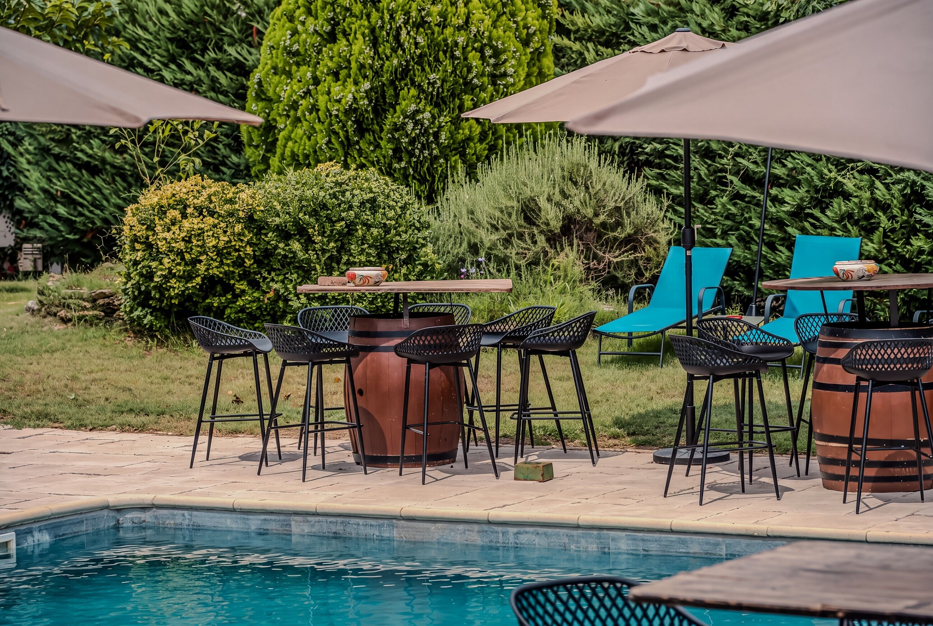 Ein Poolbereich mit Barhocker, einem Holztisch und Sonnenschirmen.