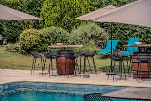 A poolside area with bar stools, a wooden table, and umbrellas.