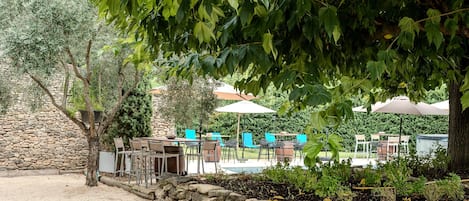 An outdoor seating area with stone walls and tables, surrounded by greenery and trees.