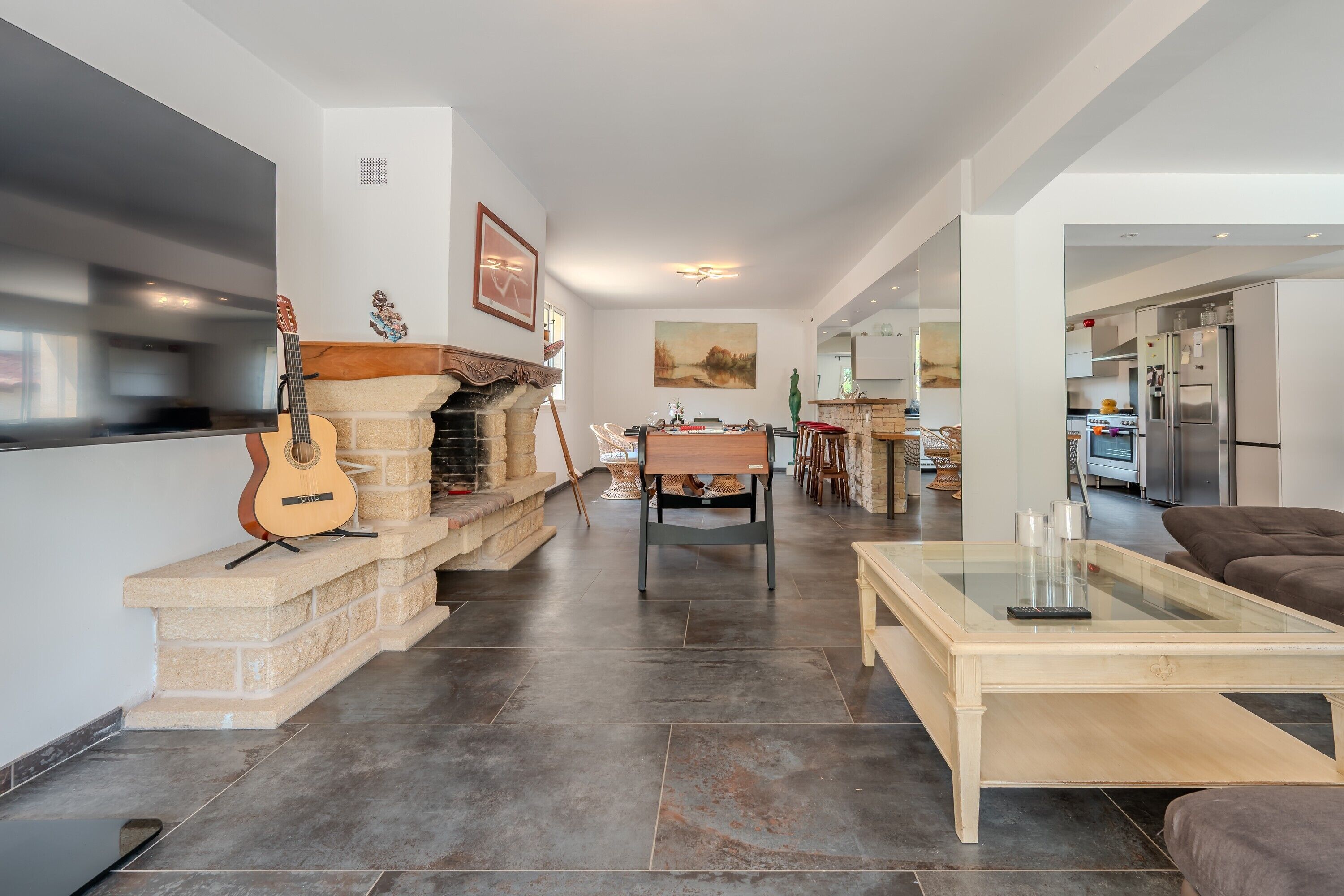 A spacious living area with a fireplace, a dining table, and a kitchen in the background.