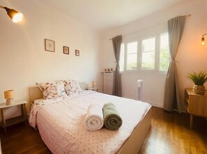 Een slaapkamer met een bed, twee nachtkastjes, een raam met gordijnen en een wandlamp.