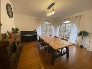 A dining room with a piano, wooden table, chairs, and large windows. - Lovely House with Splendid garden near Paris / Orly for 10-12 ppl (Épinay-sur-Orge)
