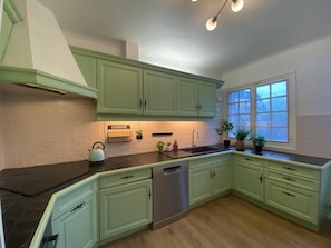 A kitchen with green cabinets, a black countertop, a dishwasher, and a window with a view. - Lovely House with Splendid garden near Paris / Orly for 10-12 ppl (Épinay-sur-Orge)