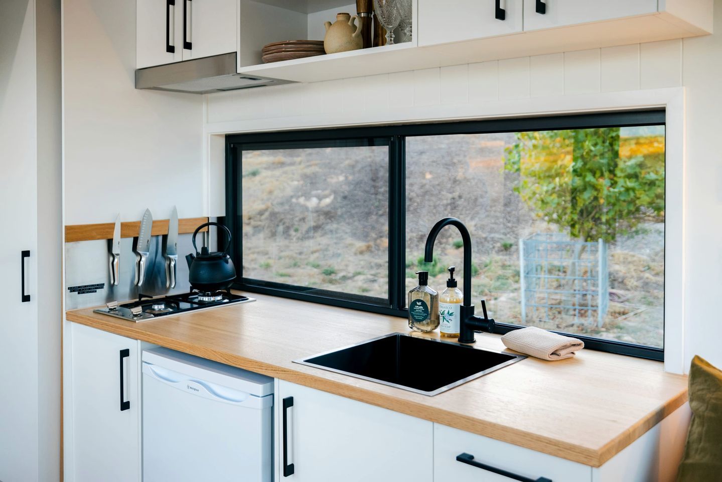 A modern kitchen with a wooden countertop, a black sink, and a window with a view of trees.