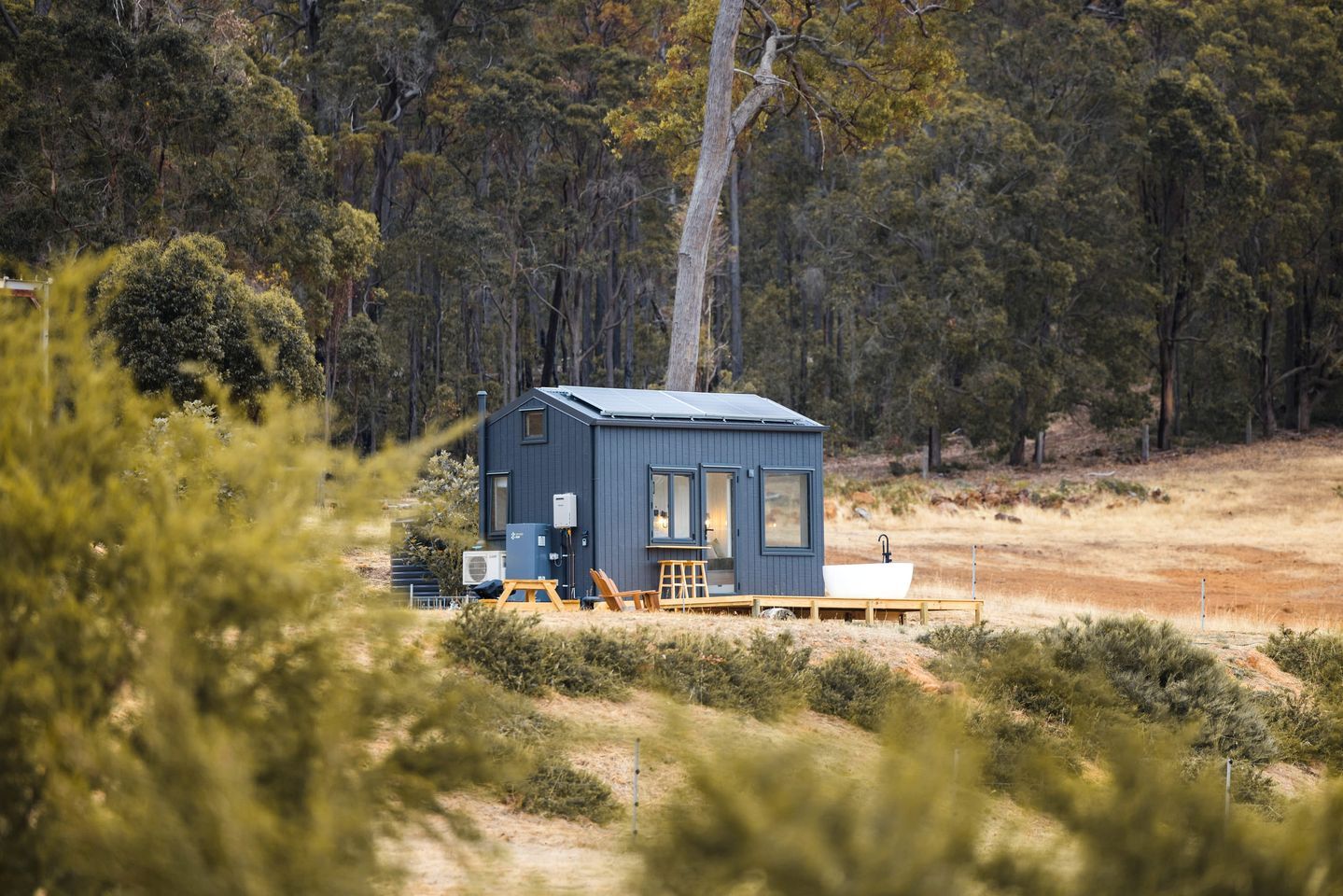 A small cabin with a deck, surrounded by trees.
