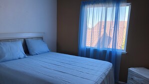 Quarto com cama, janela com cortinas finas e aquecedor fixado na parede.