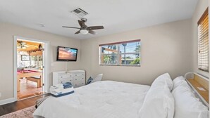 Un dormitorio con una cama, ventilador de techo, televisor y ventana con persianas.