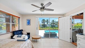 Una habitación amplia con cama, sofá, una mesa redonda y vistas a una piscina y palmeras.