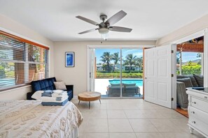 Una habitación amplia con cama, sofá, una mesa redonda y vistas a una piscina y palmeras.