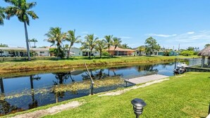 Zona residencial con una masa de agua tranquila, un área verde y una hilera de casas con un muelle.