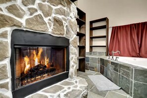 A stone fireplace with a fire, a stone shelf, a bathtub, and a red curtain. - Pet Friendly Cabin for Large Groups in the Eastern Panhandle of West Virginia, Surrounded by Scenic Nature and Historic Attractions (Berkeley Springs)