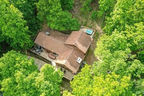A house with a large deck, a hot tub, and a covered outdoor area surrounded by dense trees. - Pet Friendly Cabin for Large Groups in the Eastern Panhandle of West Virginia, Surrounded by Scenic Nature and Historic Attractions (Berkeley Springs)