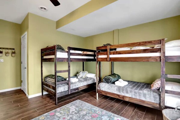 Quarto com beliche, piso de madeira, uma porta e um ventilador de teto.