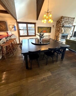 A dining area with a large round table and chairs, a chandelier, and a stone accent wall. - Pet Friendly Cabin for Large Groups in the Eastern Panhandle of West Virginia, Surrounded by Scenic Nature and Historic Attractions (Berkeley Springs)