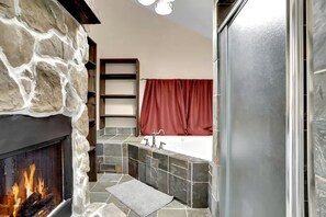 A bathroom with a stone wall, a fireplace, a bathtub, and a red curtain. - Pet Friendly Cabin for Large Groups in the Eastern Panhandle of West Virginia, Surrounded by Scenic Nature and Historic Attractions (Berkeley Springs)