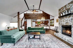 Uma sala de estar ampla com lareira, um sofá verde e uma área de jantar.