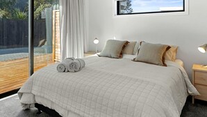 A bedroom with a large bed, two bedside lamps, and a view of a wooden deck through a glass door. - Bespoke Glamping Experiences in this Wonderful Rental in Wahihi Beach, New Zealand (Waihi Beach)