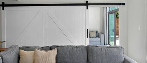 A modern living room with a grey sectional sofa, a sliding barn door, and a view of the outdoors.