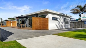 A modern two-story building with a covered patio area, a wooden fence, and a sign for Tasman Holiday Parks. - Bespoke Glamping Experiences in this Wonderful Rental in Wahihi Beach, New Zealand (Waihi Beach)