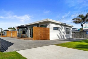 A modern two-story building with a covered patio area, a wooden fence, and a sign for Tasman Holiday Parks.