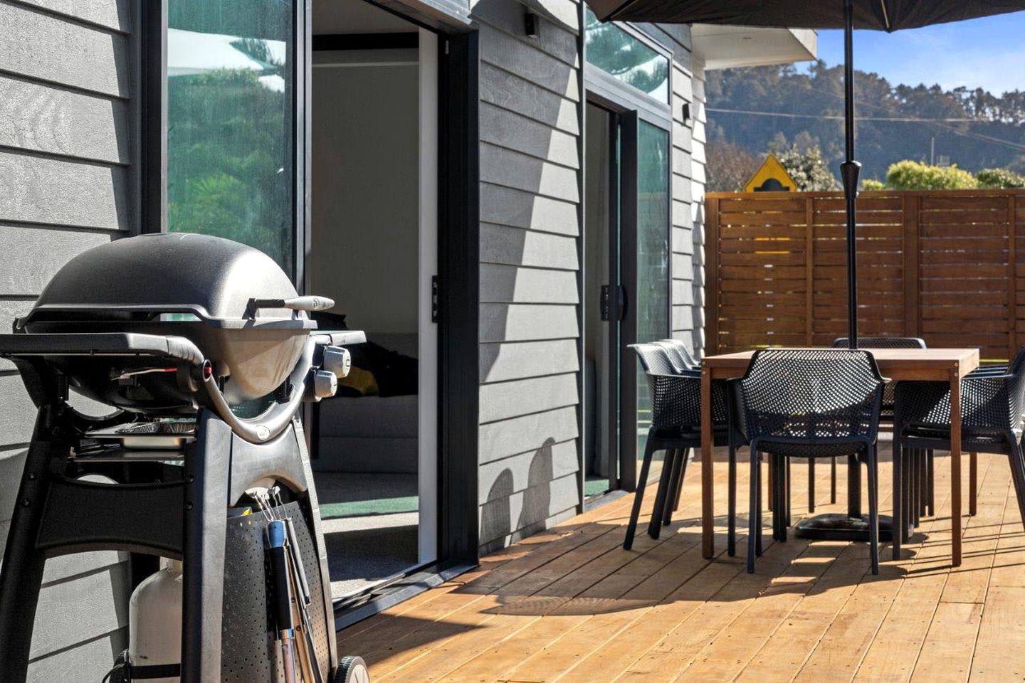 An outdoor patio with a barbecue grill, a table with chairs, and a wooden fence in the background.