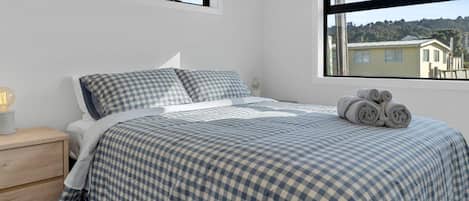 Un dormitorio con una cama, dos ventanas, una mesita de noche y una lámpara.