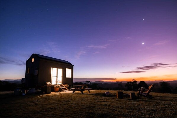 Une maison de plain-pied dotée d’une grande fenêtre, d’une terrasse avec une table et des chaises, et offrant une vue sur le paysage.