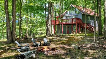 A cabin with a red porch, surrounded by trees, and a fire pit with chairs.
