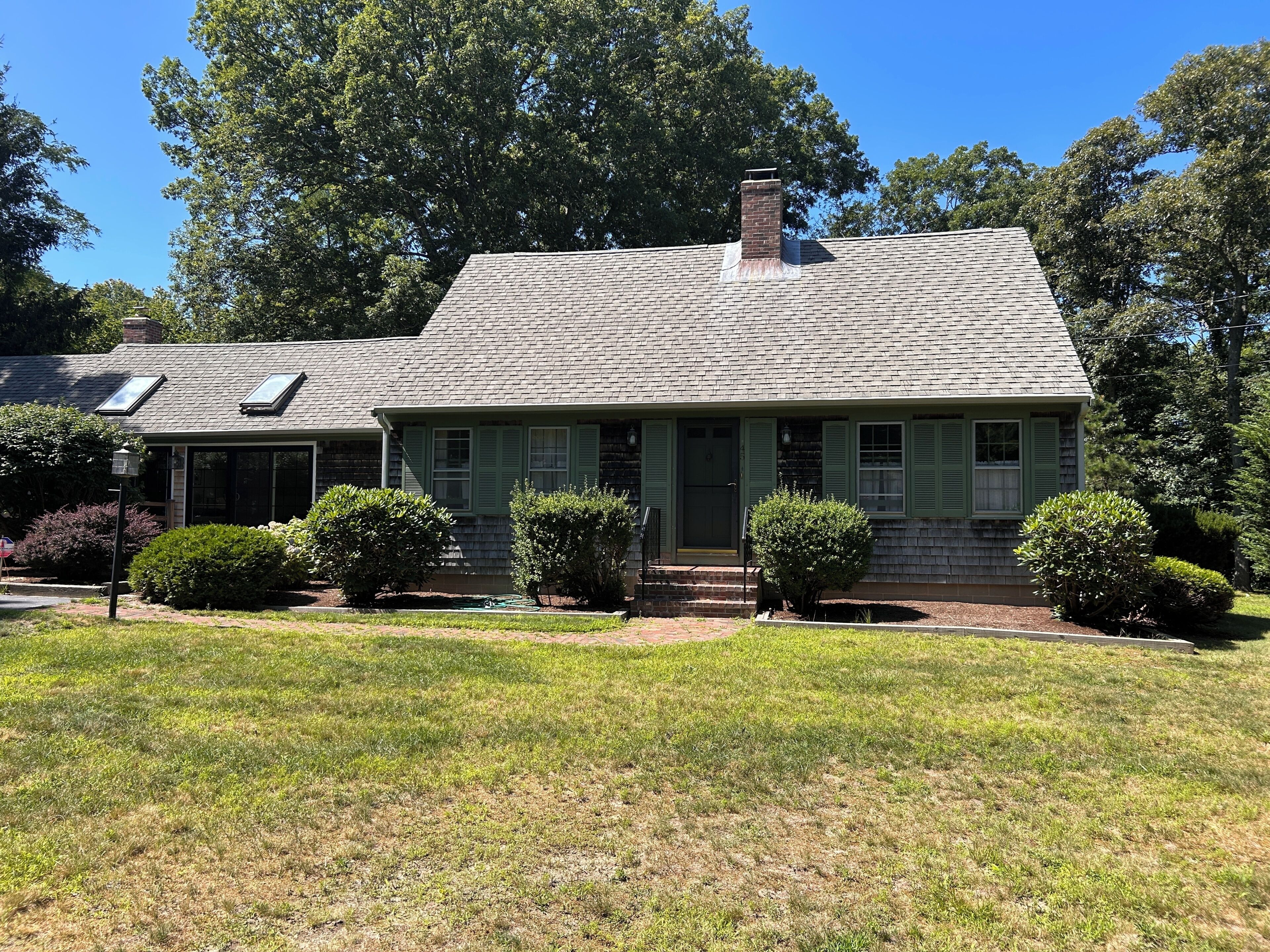 A two-story house with a sloped roof, a chimney, and a front porch with green shutters.