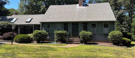 A two-story house with a sloped roof, a chimney, and a front porch with green shutters.