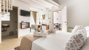 A modern hotel room with a large bed, a desk, a chair, a TV, and a bathroom. - Domus Sagari - Junior Suite (Presicce)