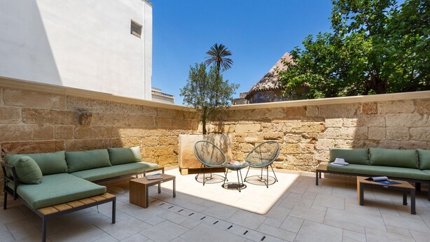 A courtyard with a green sofa, two chairs, a small table, and a stone wall. - Domus Sagari - Junior Suite (Presicce)