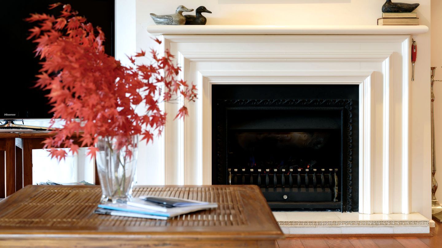 A fireplace with a mantel, a vase with red foliage, and a table with a book and a pen.