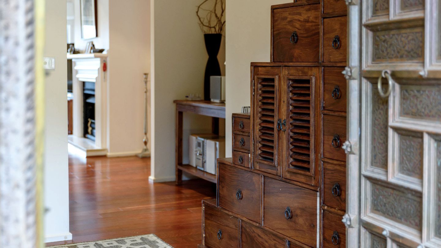 A wooden dresser with multiple drawers and a mirror, positioned in a hallway with a wooden floor and a rug.