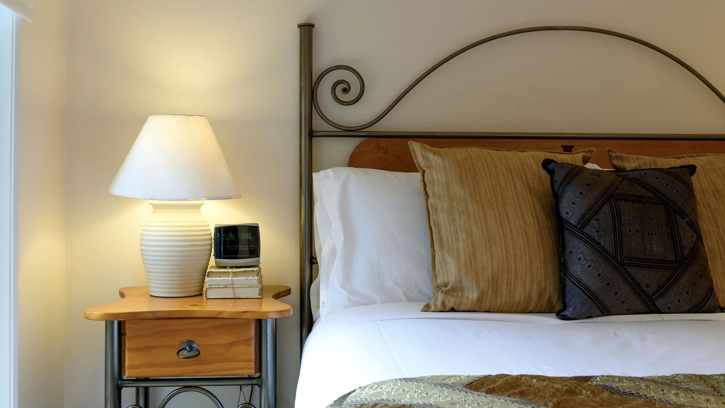 Un lit bien fait, avec une tête de lit, une table de chevet sur laquelle se trouve une lampe, et une pile de livres.