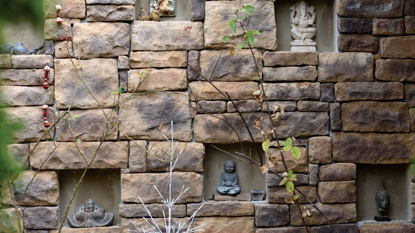A stone wall with multiple niches containing statues and a Buddha figure.