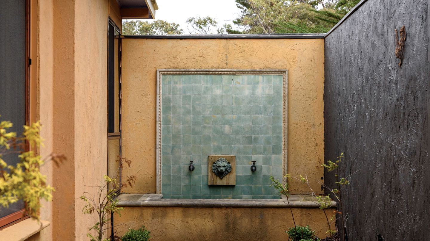 A small outdoor water feature with a square tile wall and two spouts.