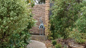 Ein Garten mit Steinmauer, Metallskulptur und verschiedenen Pflanzen.