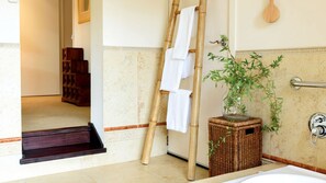 Une salle de bain avec une baignoire, un porte-serviettes en bois, un panier en osier contenant une plante et un escabeau en bambou.