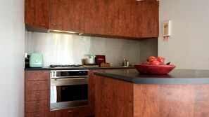 Eine Küche mit Holzausstattung, einem Edelstahlbackofen, einem grünen Gerät und einer roten Fruchtschale auf der Arbeitsplatte.